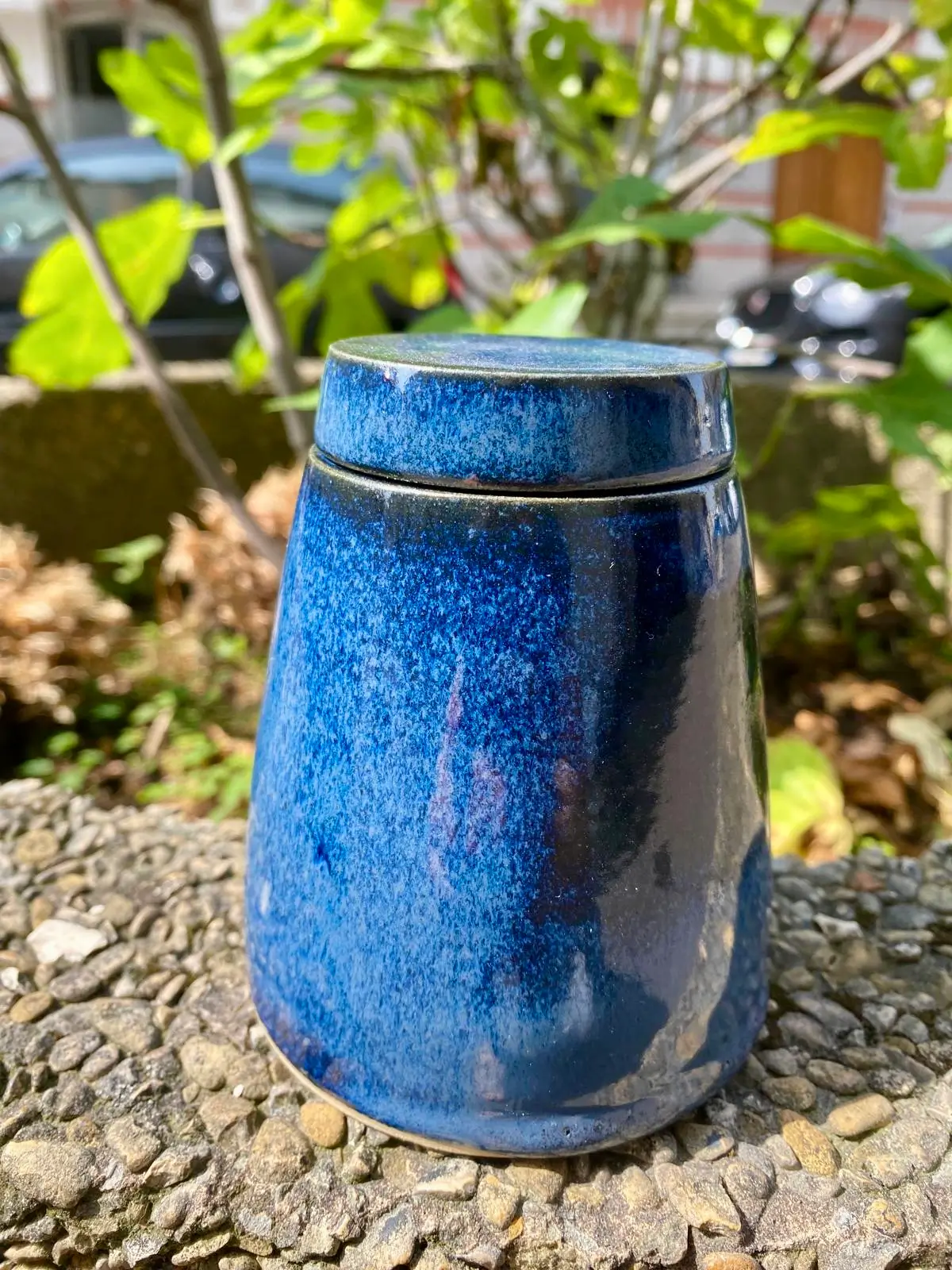 Pot couvert en céramique émaillée bleu moucheté, photographié en extérieur